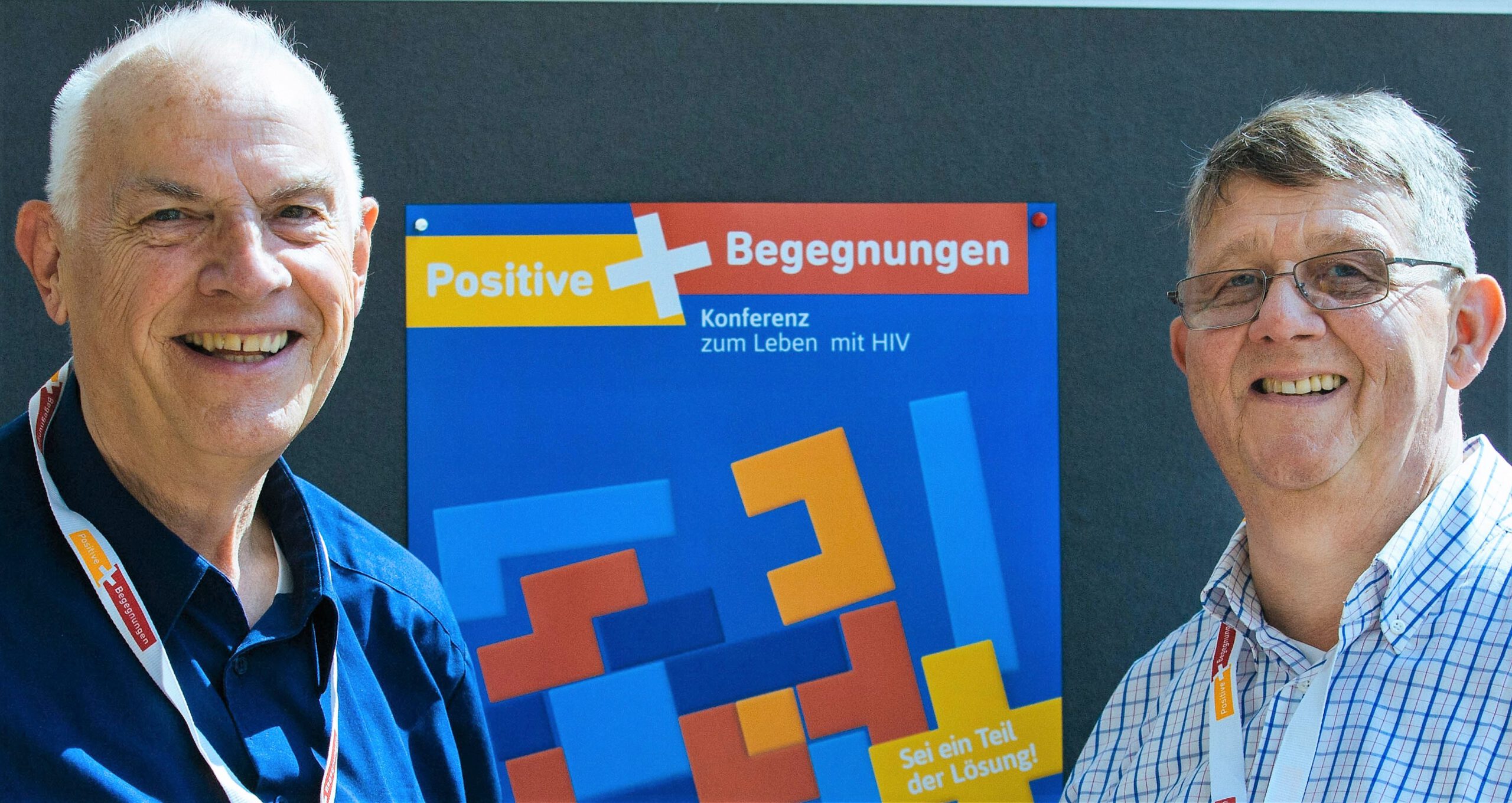 Georg Roth und Sigmar Fischer, beide Vorstände der Bundesinteressenvertretung schwuler Senioren, vor dem Veranstaltungsplakate der Positiven Begegnung.